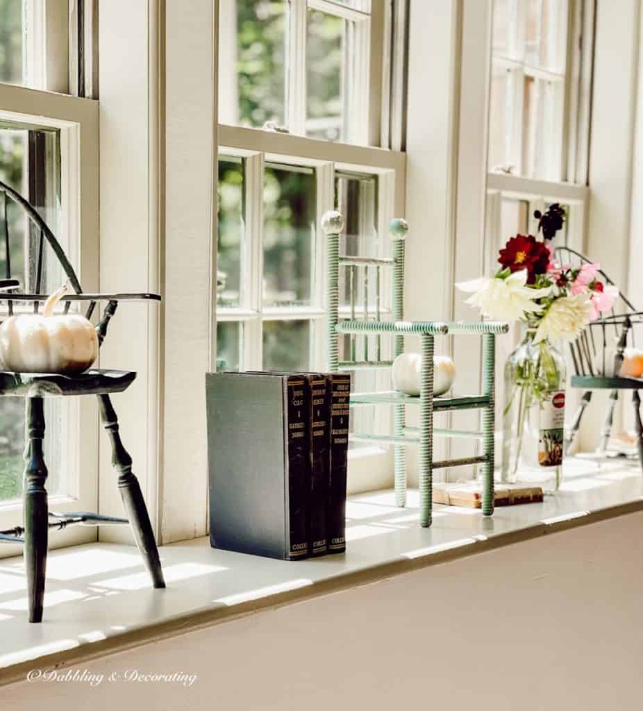 windowsill with pumpkins and doll chairs.