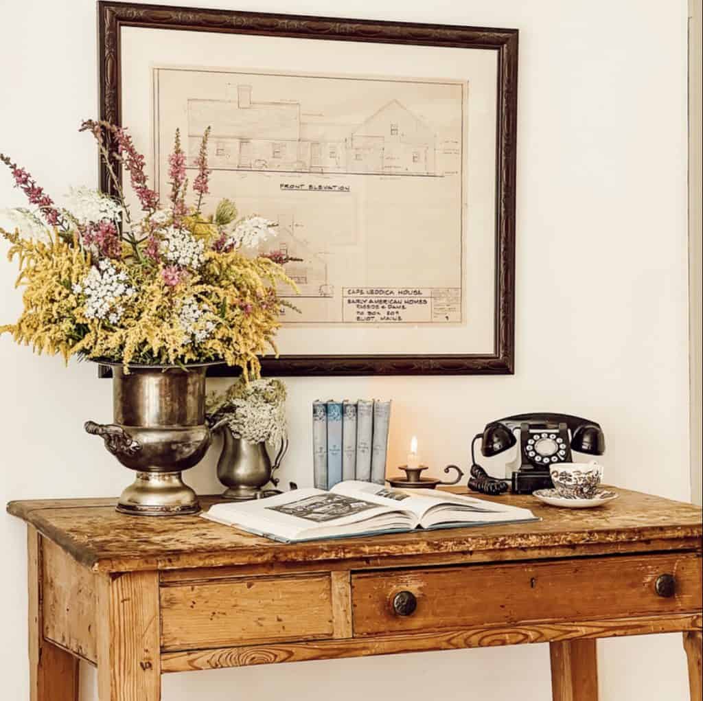 A vintage desk adorned with a vase of flowers and a telephone, creating a thrifty yet stylish decorating solution.