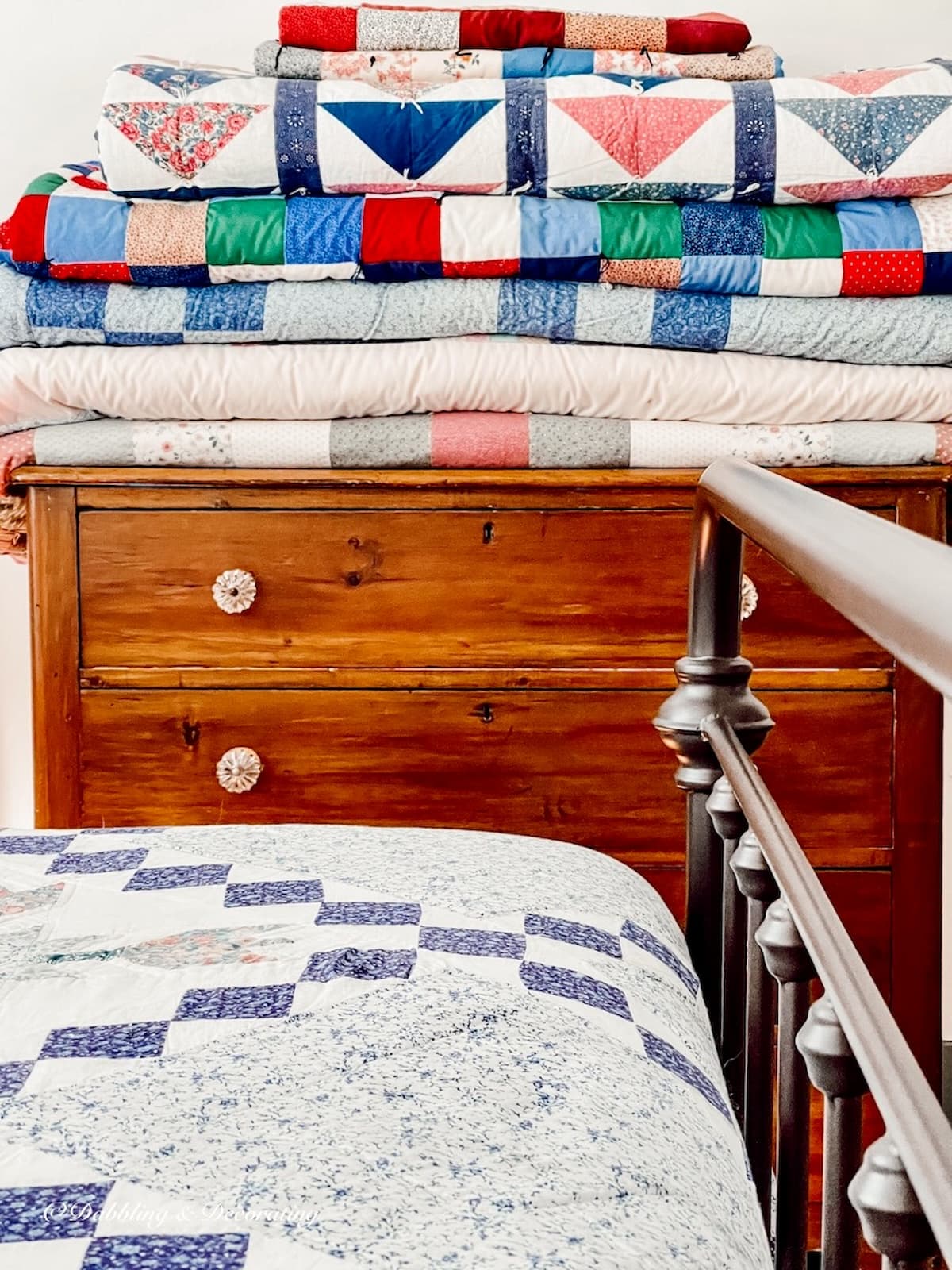Display of folded vintage quilts on bedroom dresser. Vintage aesthetic bedroom.