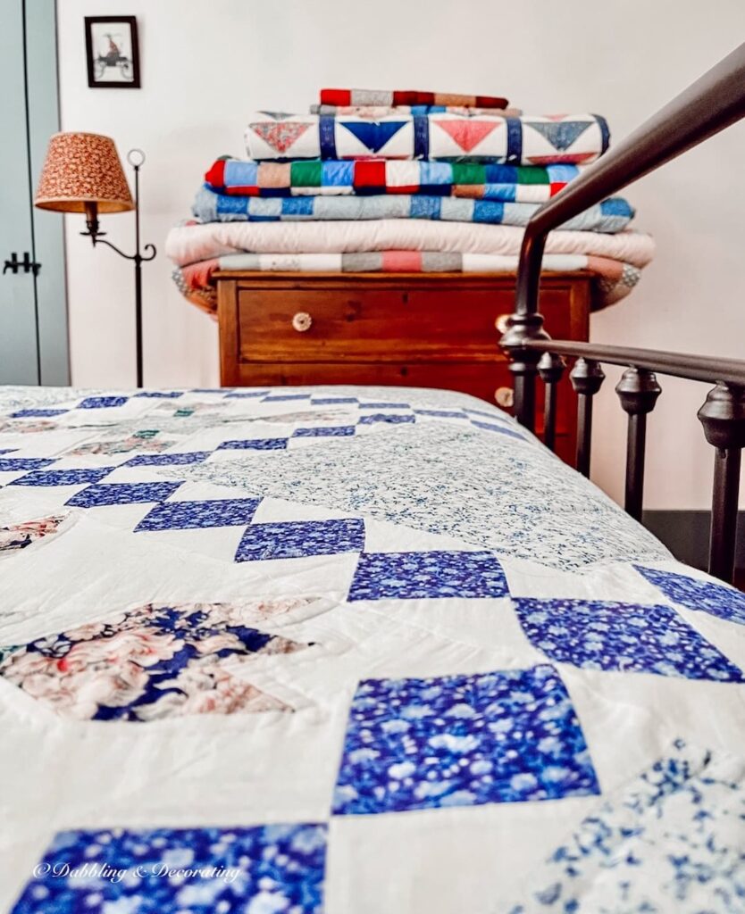 Display of folded vintage heirloom quilts on bed and bedroom dresser in vintage style.