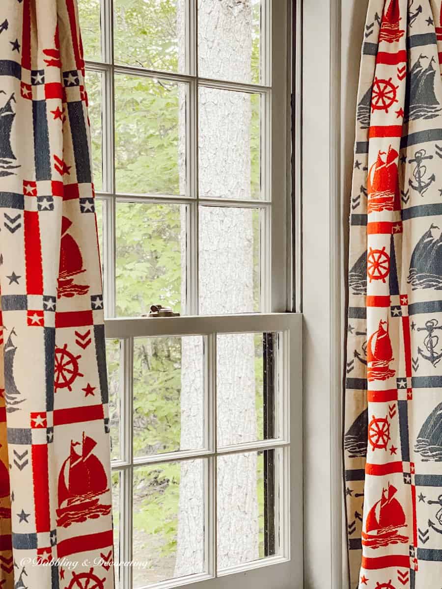 Vintage coastal curtains on window in red and blue with sailboats and anchors in Antique styled Maine home.