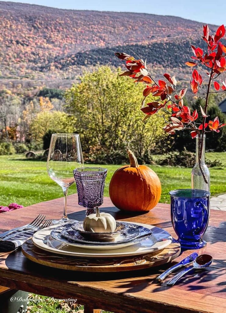 Outdoor front porch table place setting with blue and amethyst glassware, vintage place setting and pumpkin with mountain views for fall.