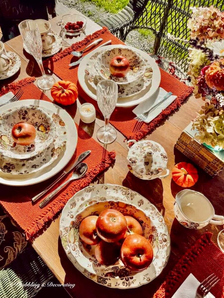 Outdoor fall tablescape with Johnson Brothers Autumn's Delight dinnerware on outdoor porch table with pumpkins.