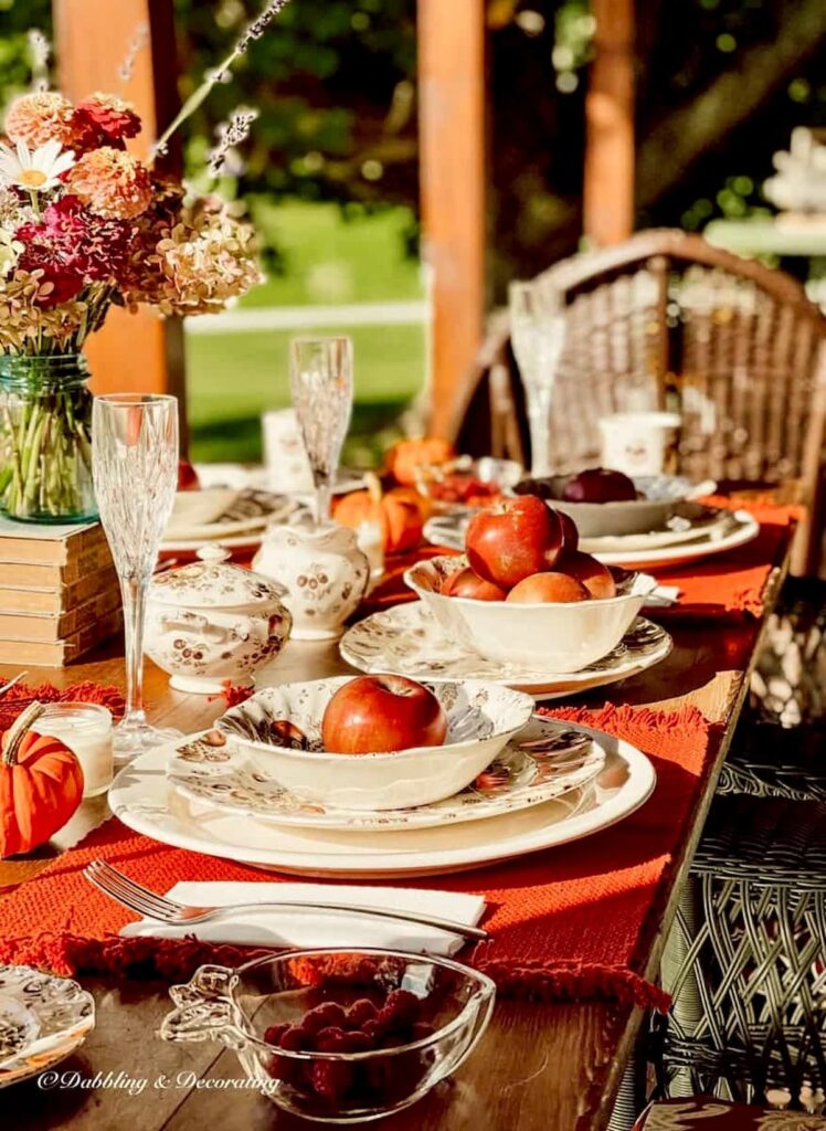 Autumn themed dinnerware with Johnson Brothers table setting on outdoor porch table with flowers and pumpkins.