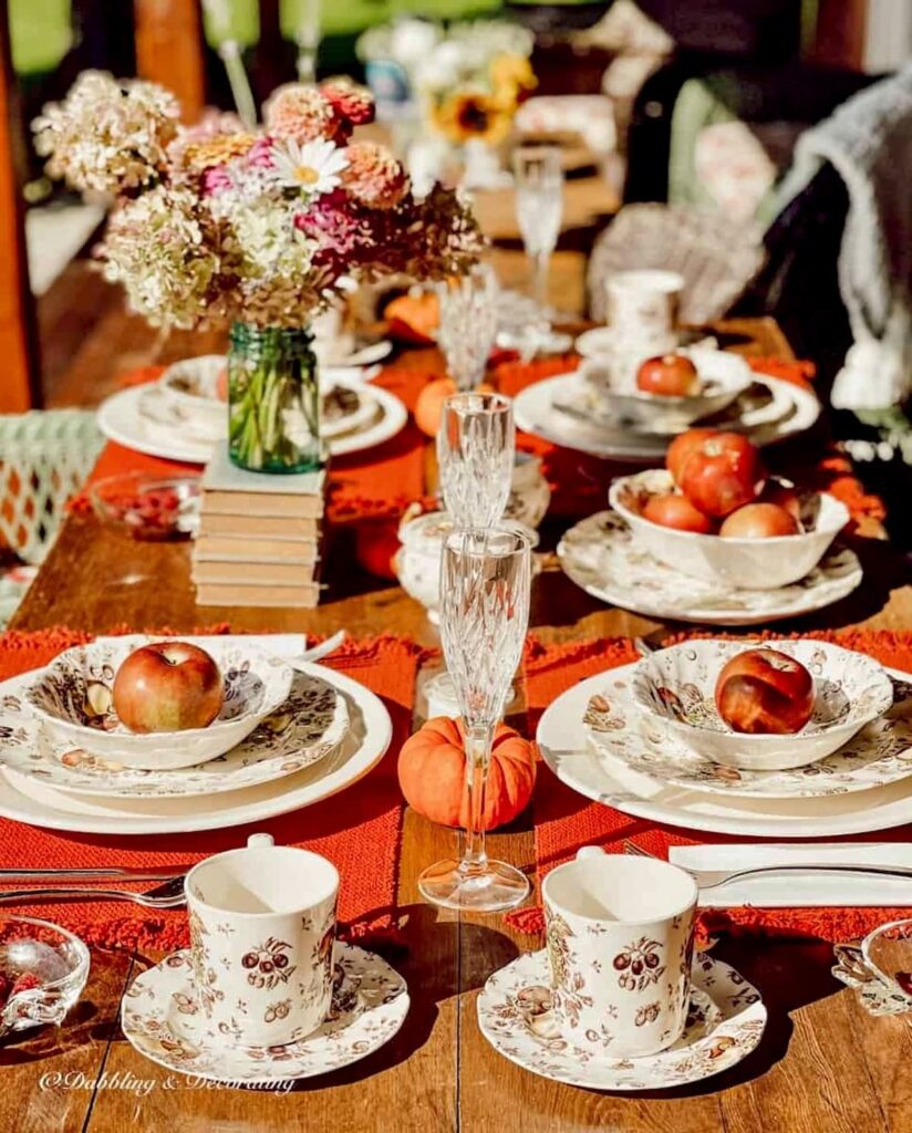 Autumn themed dinnerware with Johnson Brothers Autumn's Delight with pumpkins, flowers, and red placemats on outdoor porch table.