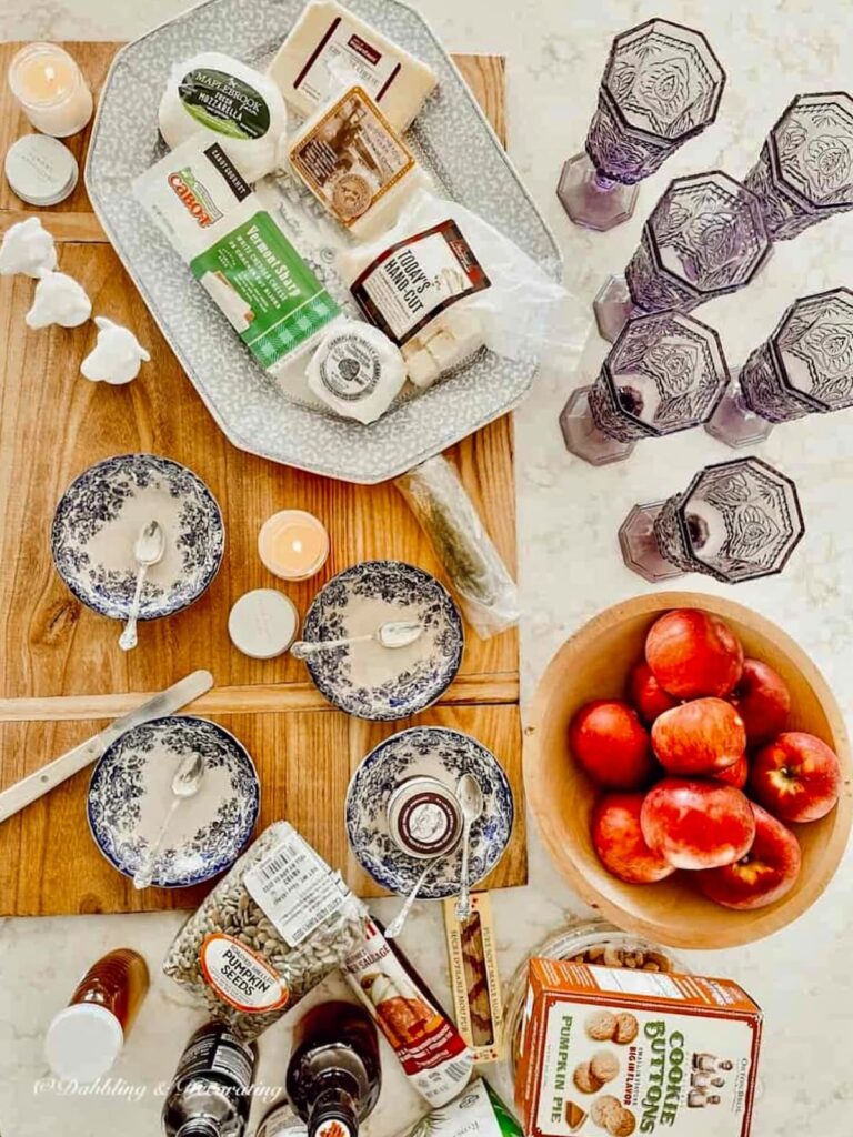 Vintage platter on cheese board with scattered vintage bowls, apples and cheeses with amethyst glassware paired.