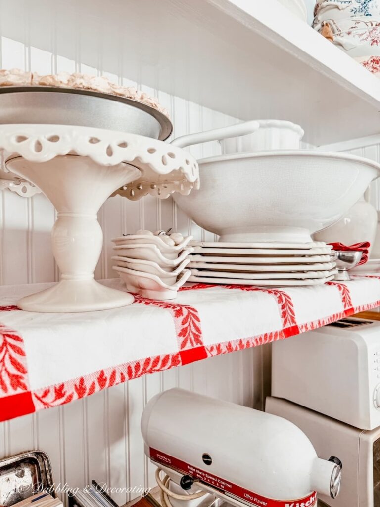 Vintage open kitchen ideas with white open shelving with red and white vintage tablecloth paired with white ironstone.