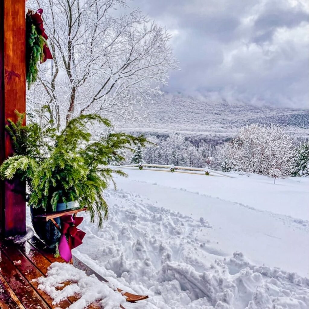 Vintage ski house decor with evergreens and porch wreath overlooking Vermont mountains with a large dumping of snow, gorgeous scenery.
