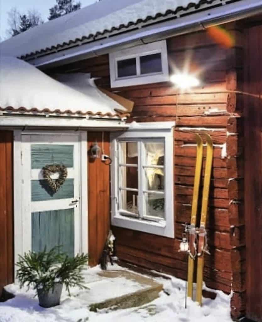 Swedish home red, with blue door and yellow skis in snow.