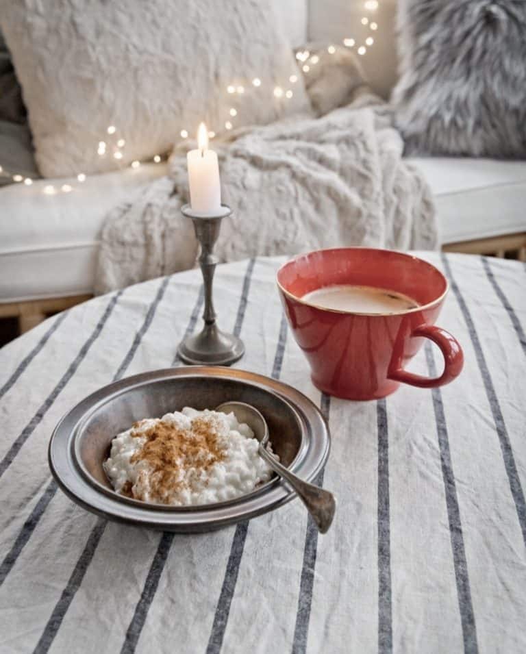 Red coffee mug, oatmeal and pewter candlestick lit in cozy breakfast nook.