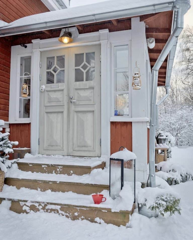 Winter Red Swedish Homes in the snow with light on and red coffee mug on outdoor step.