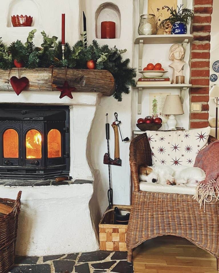 Swedish country fireplace with cozy Christmas decor details and dog curled upon chair.