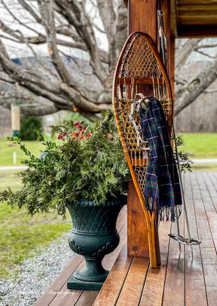Vintage snowshoes on porch beam with green and blue scarf with urn of evergreens.
