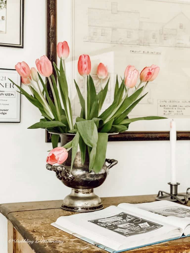 Pink tulips in vintage vase standing tall except one.