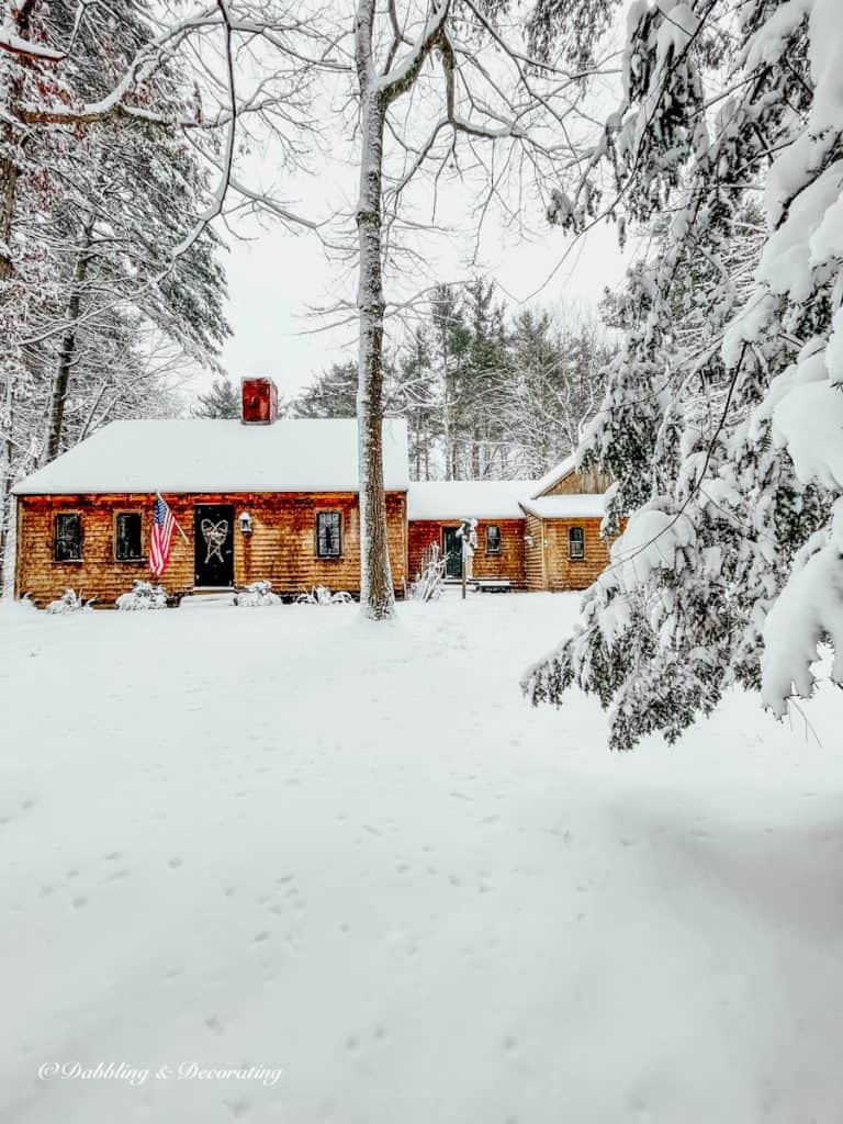 Cozy Snow Day at Home at our home in Maine.  Cedar shakes siding in the woods during snow storm.  American flag and vintage snowshoes on front door.