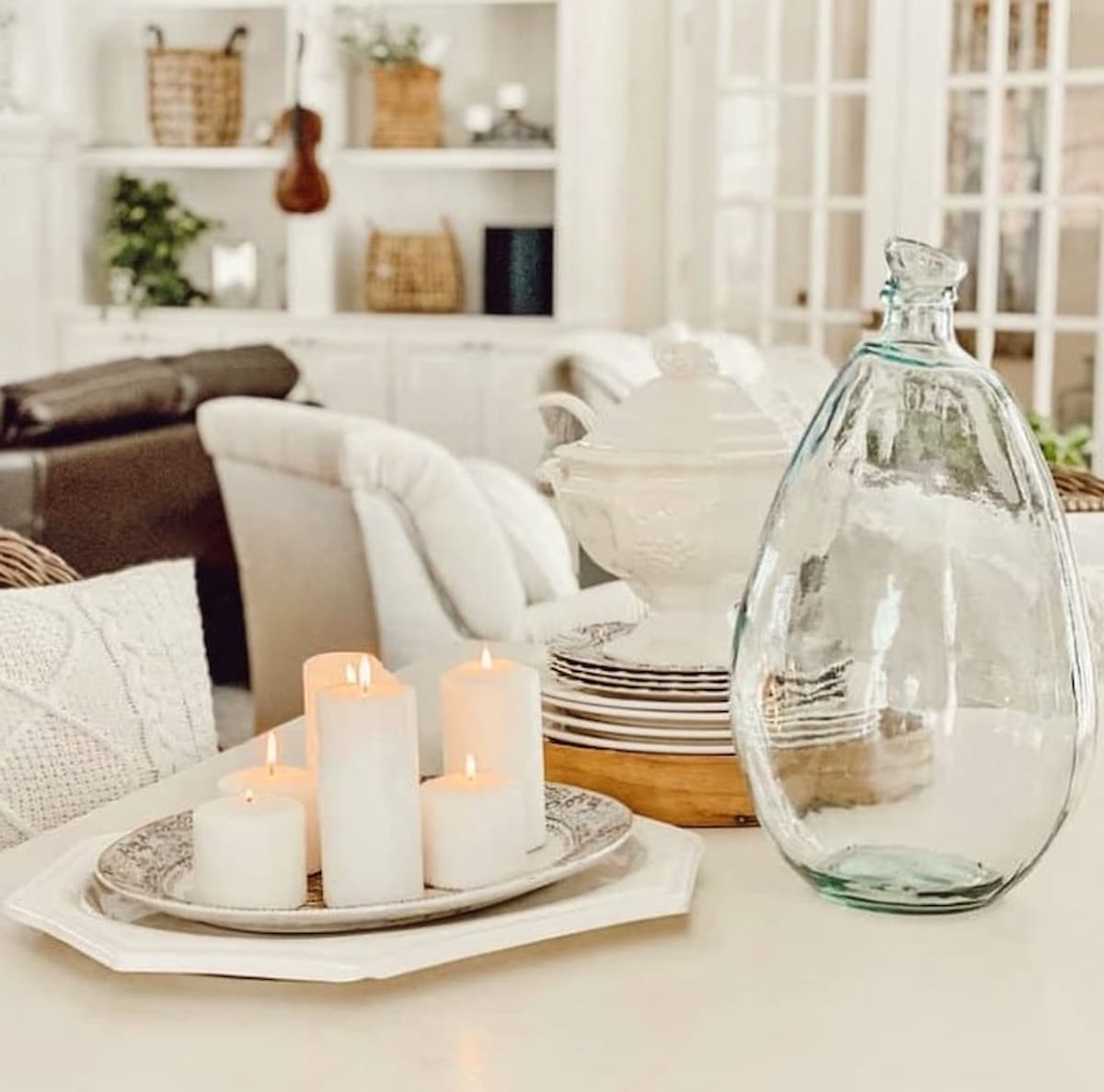 Cozy snow day at home dabbling and decorating with vintage finds. A platter of white candles, bottle and soup tureen gathered on white farmhouse table.