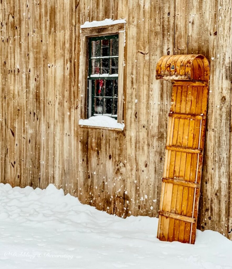 How to decorate a vintage sled with a toboggan leaning up against a snowy cedar shake home.