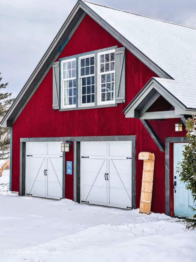 Red barn garage with a decorative vintage sled leaning up against the side in the snow.