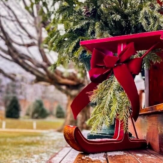 Vintage red Jack jumper sled with red bow on porch step with evergreens in how to decorate a vintage sled.