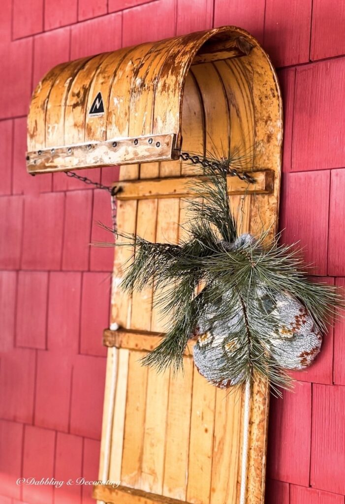 How to decorate a vintage sled with a wooden toboggan and handmade mittens tied with evergreens.