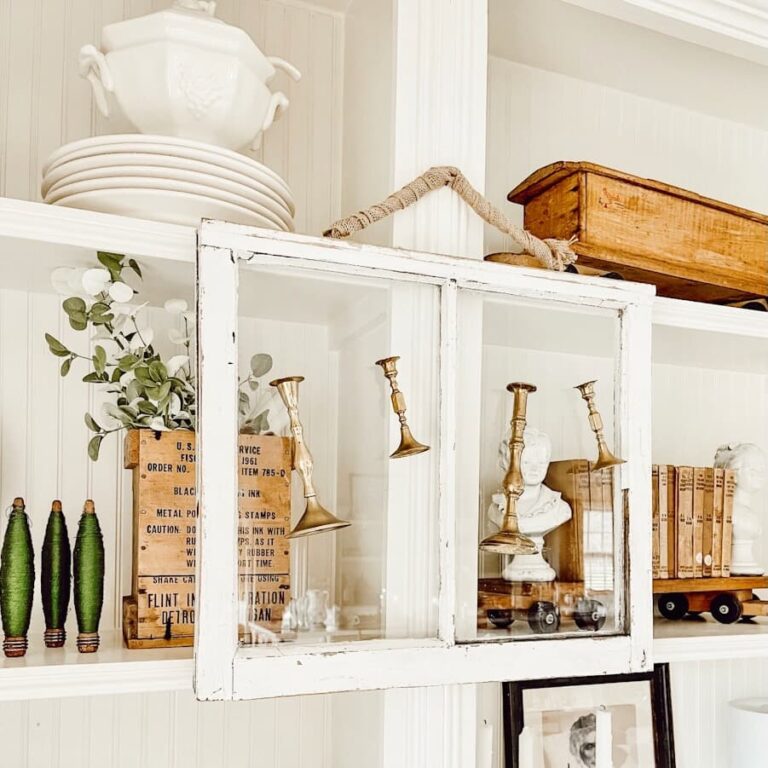 Vintage brass candlesticks hanging from a white salvaged window on vintage style bookcase in salvaged window decor ideas.