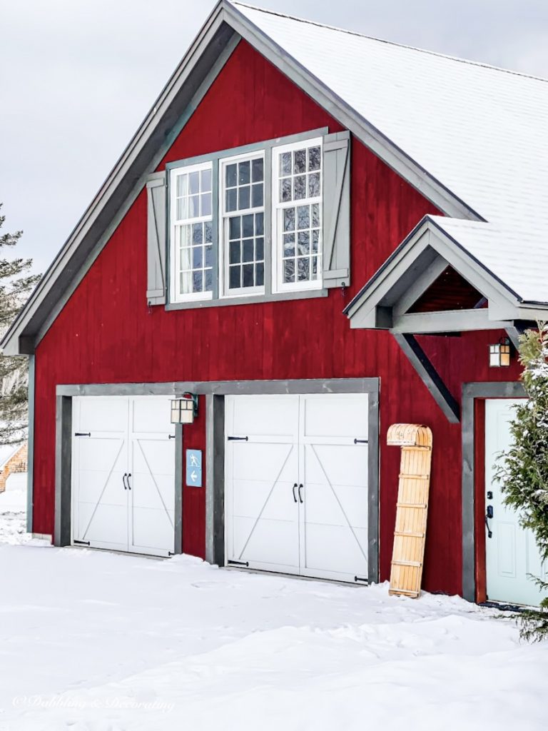 Vintage wooden sled leaning up against red barn in the snow.