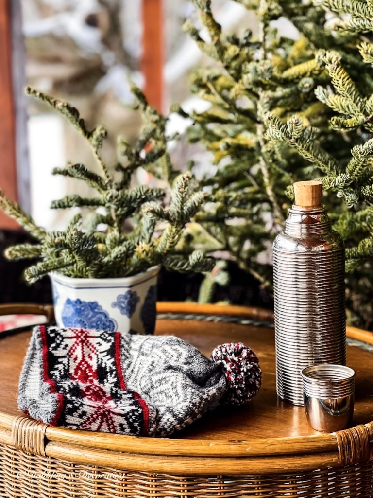 vintage style ski hat, vintage thermos and evergreens on porch table.