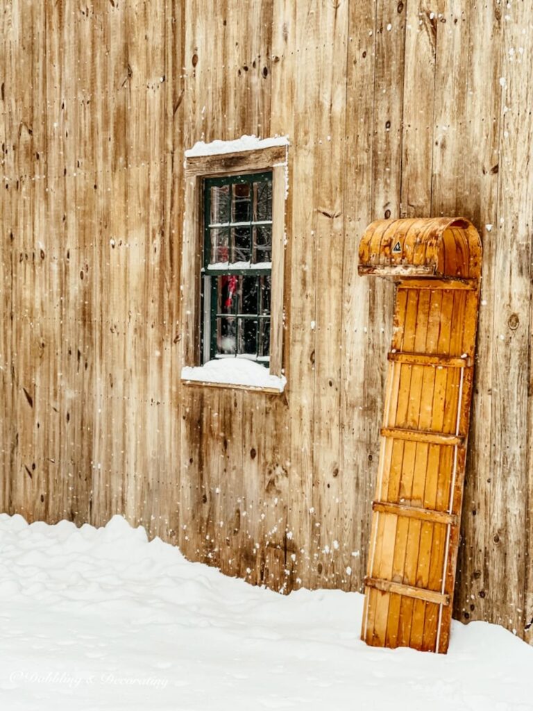 Vintage sled decor with toboggan in snow leaning up against cedar shakes barn.