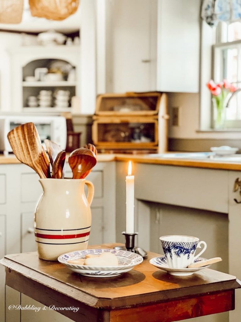 Country Kitchen vintage table island with crock of wooden utensils, dishes, and lit candle.