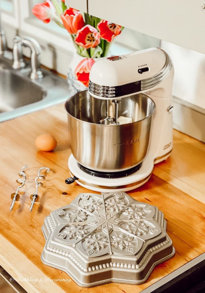 Kitchen mixer on wooden kitchen counter top with flowers and cooking supplies.