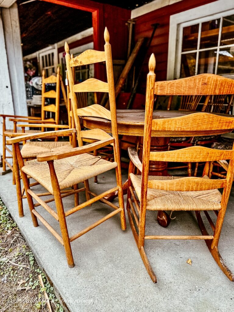 A collection of antique style chairs, ladder backs in different styles outside of a barn sale.