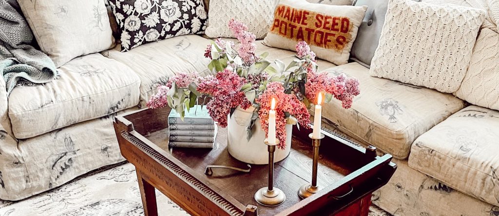 A vintage coffee table decorated with flowers and candles with brass candlesticks, thrift store decor ideas.
