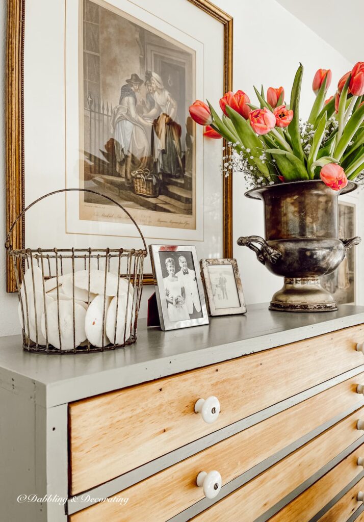 Vintage hutch styling ideas with flower bouquet, basket of sand dollars and family photos in sunroom.