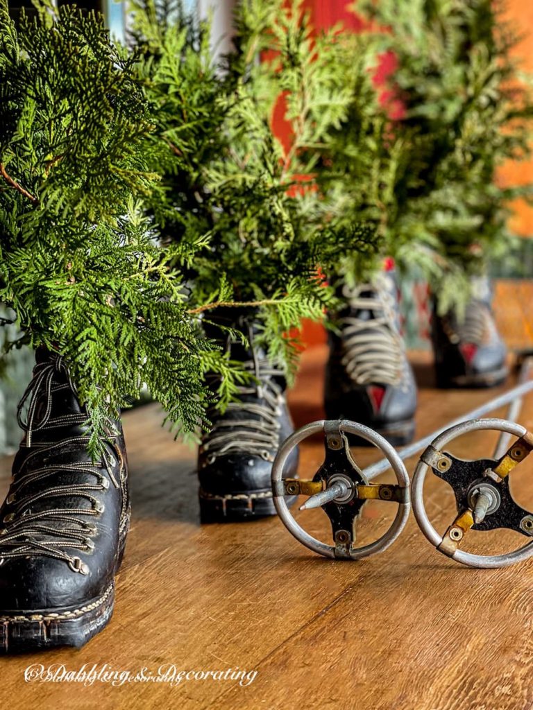 Vintage ski boots with evergreens and ski poles on table.