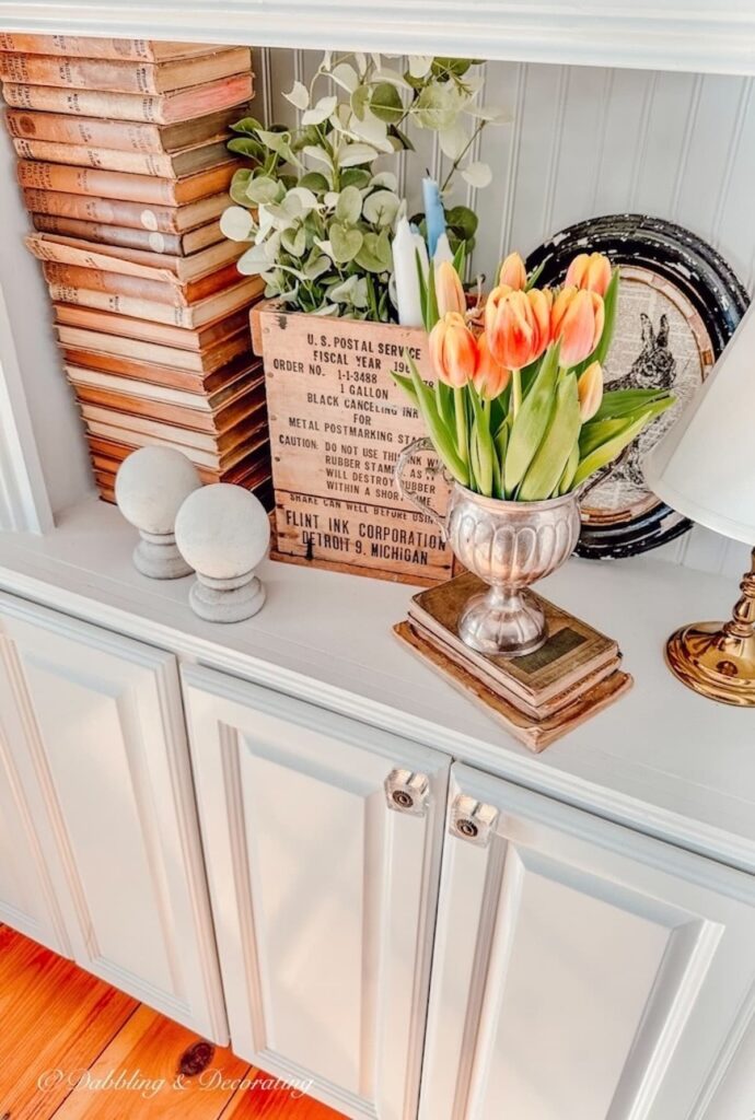 Orange Tulip Arrangement in silver vase on bookshelf