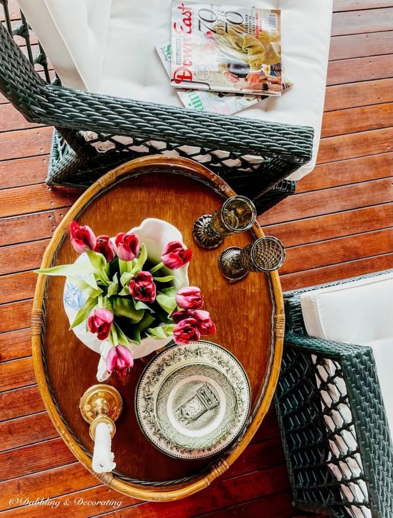 Vintage wicker side table with flowers and glasses next to green wicker furniture on back porch.