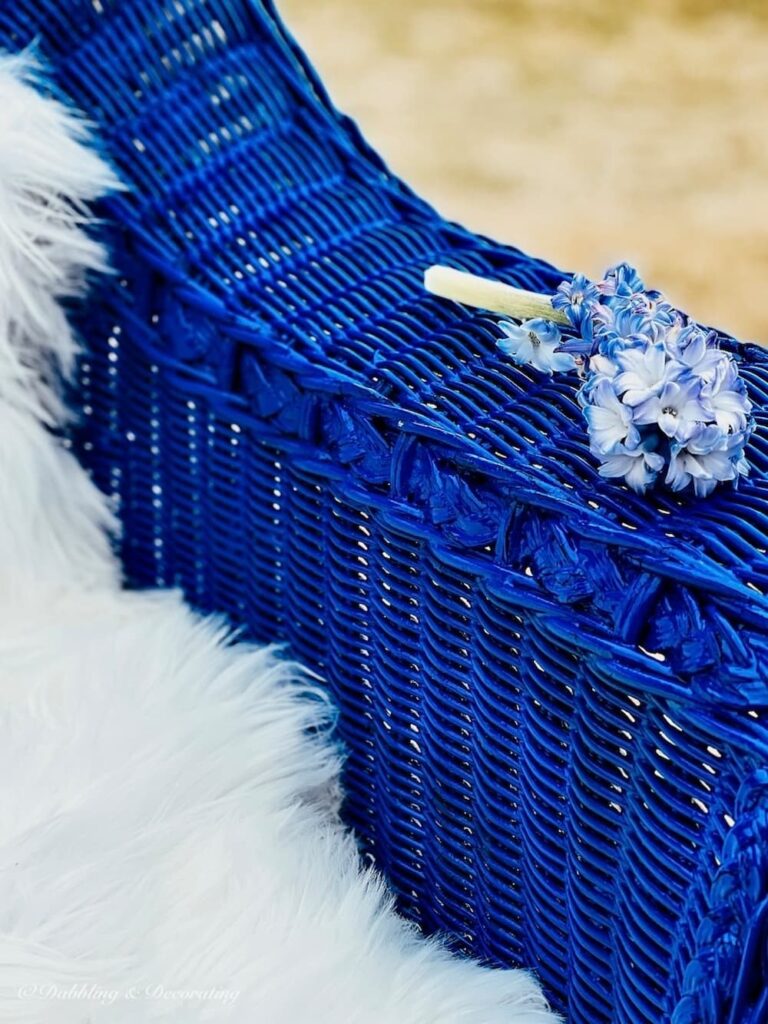 Blue painted arm of wicker chair with sheepskin and lilac branch.