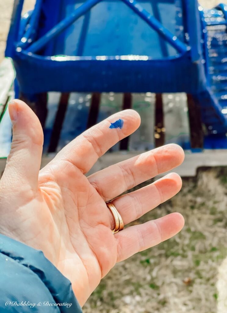 hand with blue paint on it while how to paint wicker furniture tutorial.