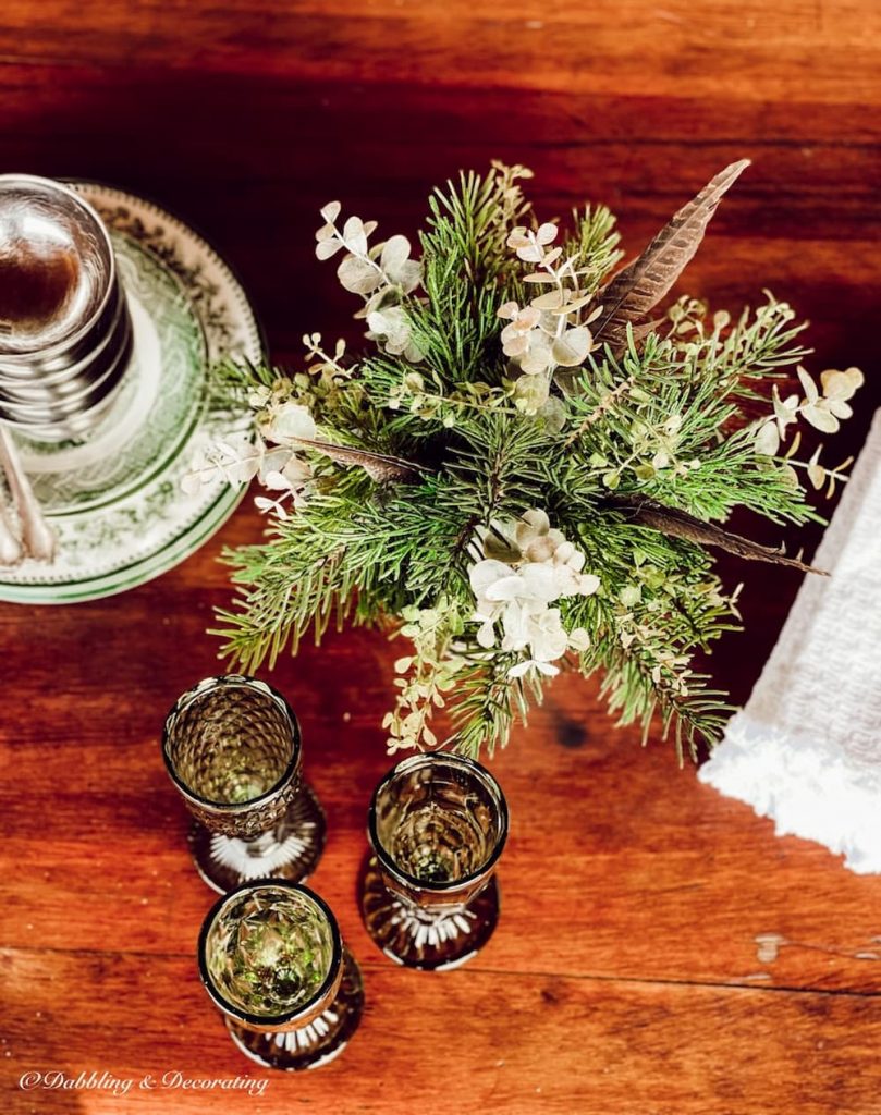 Greenery, glassware and dishes on refinished wooden table.