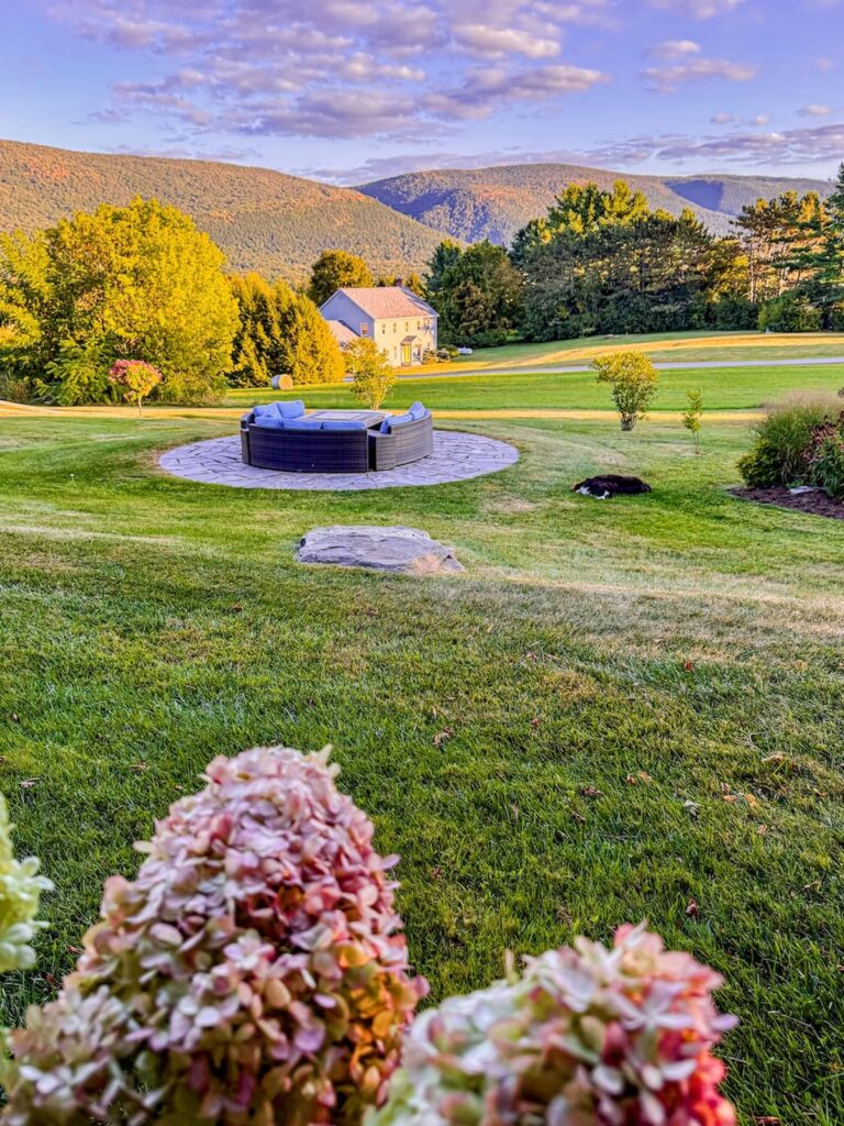 Backyard fire pit and patio with sectional seating with Vermont mountains and pink hues during fall.