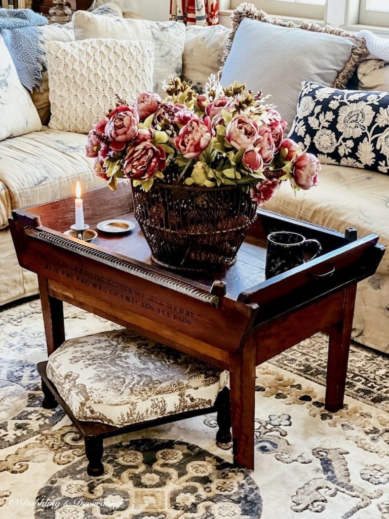 Vintage coastal coffee table styled with faux peonies and rustic basket.