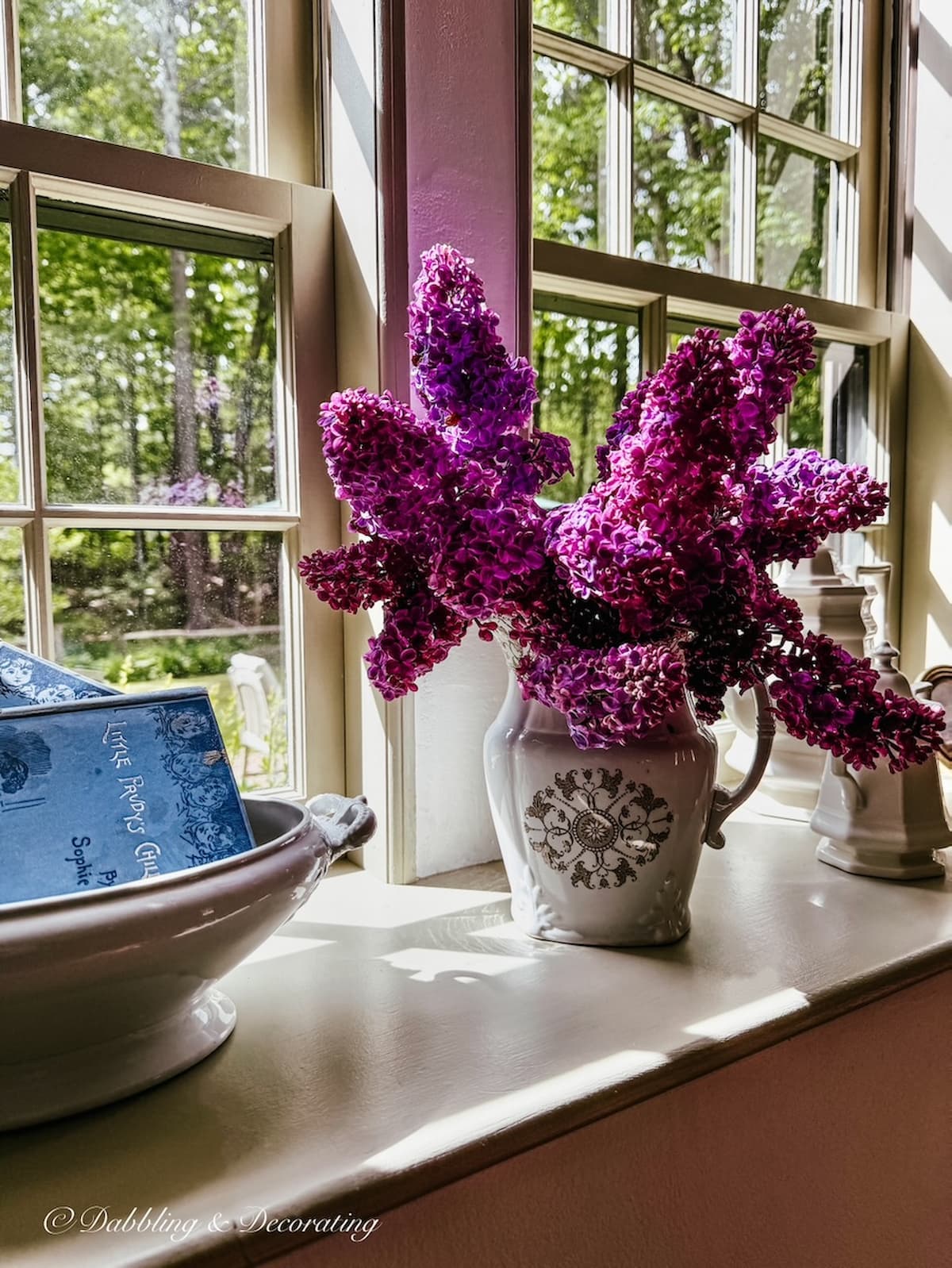 Lilac flower bouquet in brown and white transferware pitcher on moody window sill.