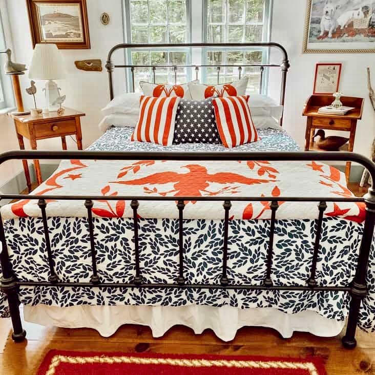 Wrought iron bed styled with red, white, and blue vintage Americana decor ideas with quilts and antique furnishings in small guest bedroom in New England home.