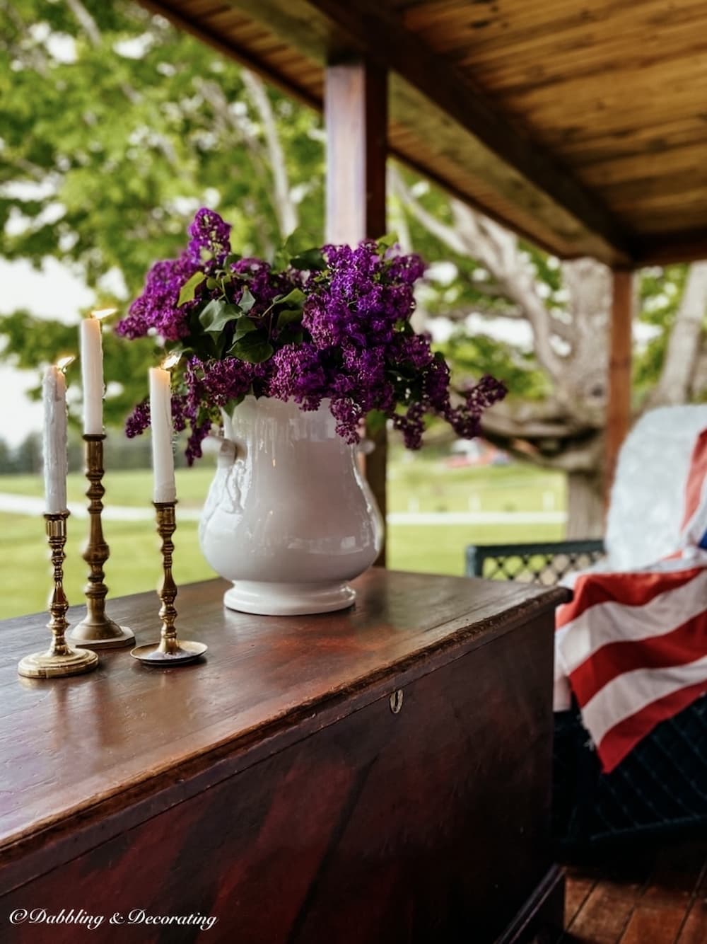 Simple Vintage Americana decor ideas on covered porch with lilacs, candles, and draped USA flag.