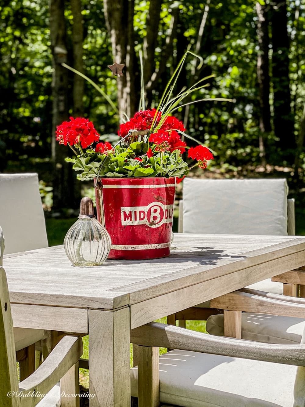 Vintage Red bucket with red geraniums on table.