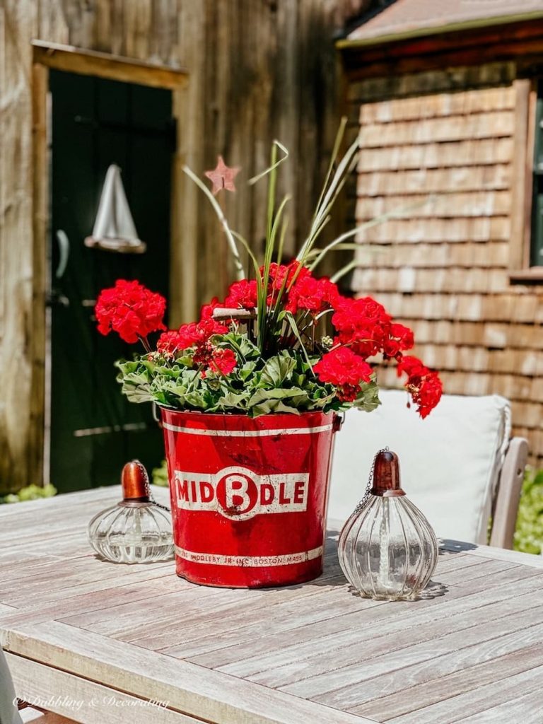 Vintage Red bucket with red geraniums on table.