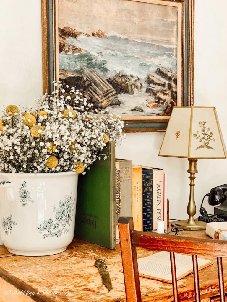 Vintage blue and white large transferware bowl with dried flowers on desk with books and a lamp and seaside painting.