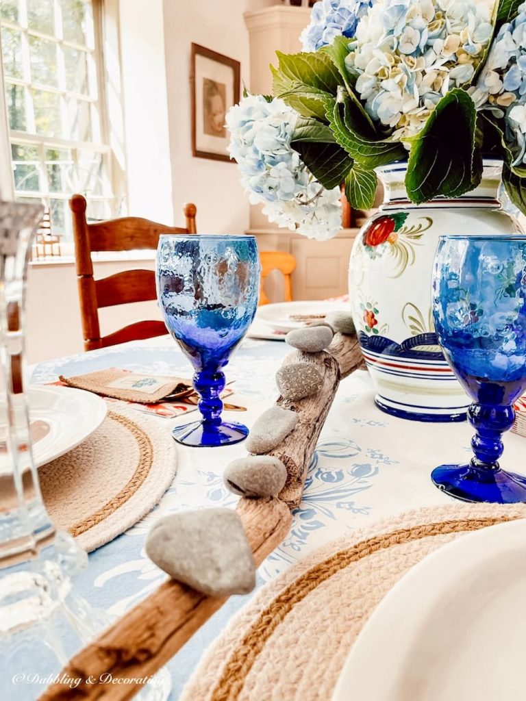 Blue glassware, driftwood and rocks on lobster decor table setting.