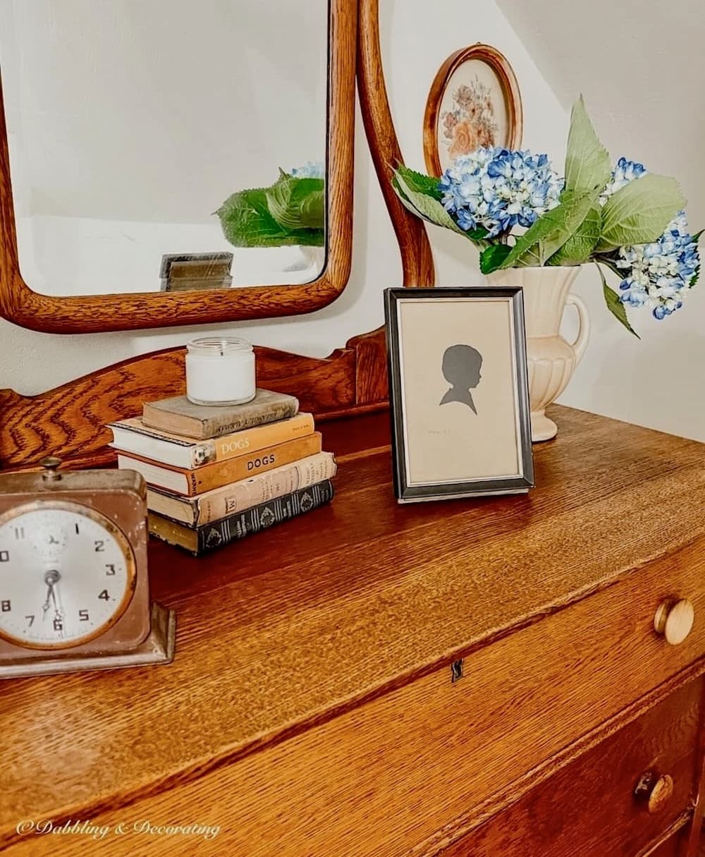 Antique oak dresser styled with a mirror in old-fashioned attic bedroom with old books, alarm clock, and more.
