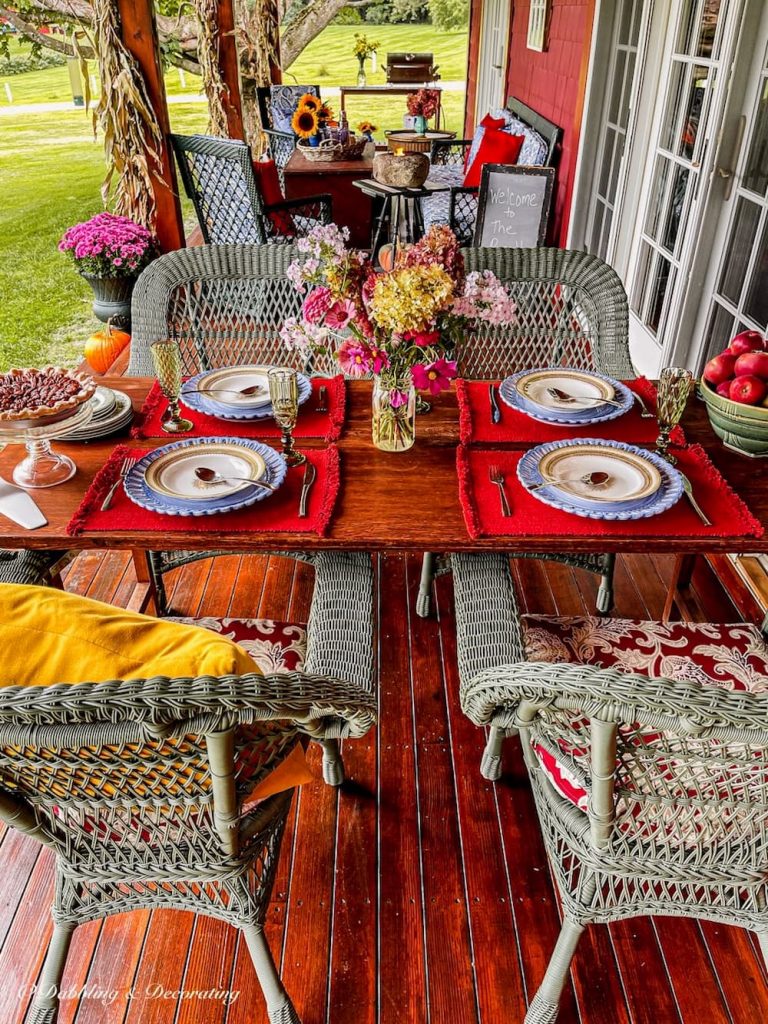 Fall porch table setting with urns of purple mums, corn stalks and colorful styling.